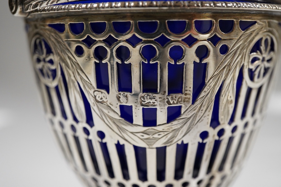 Two George III pierced silver pedestal sugar baskets, with blue glass liners, spiral handle, Burridge Davenport, London, 1777, the other William Plummer, London, 1775, tallest 10.1cm excluding the handle.